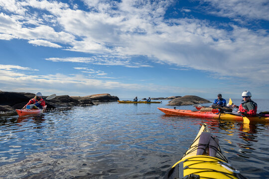 Sea kayakers regrouping among granite islets under a wide blue sky with copy space, seen from a yellow kayak bow, Georgian Bay, Ontario, Canada