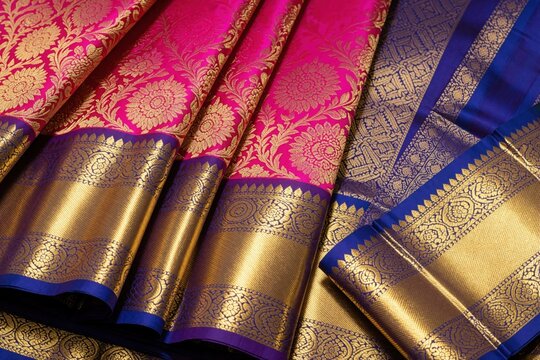 Pink Kanchipuram pattu silk saree with gold zari border. Traditional Indian ethnic wear features intricate floral motifs, heavy metallic weave. Luxury bright textile fabric displays rich texture,