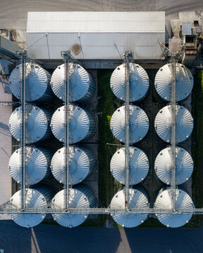 Aerial view of industrial grain silos arranged in a grid pattern with metallic surfaces and shadows in Slesin, Greater Poland Voivodship, Poland.