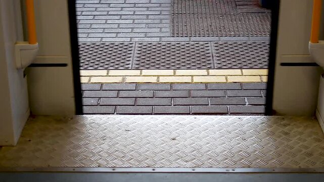 Public transit train doors closing at a station platform with tactile paving and yellow safety line visible from inside the vehicle interior