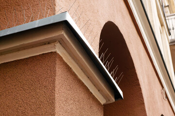 Low angle view of anti bird spikes installed on a building facade corner cornice for pest control protection outdoors © MarijaBazarova