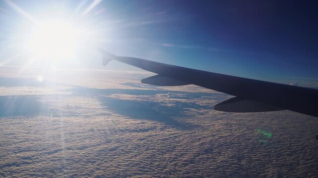 Airplane Wing Above Clouds with Bright Sunlight and Lens Flare