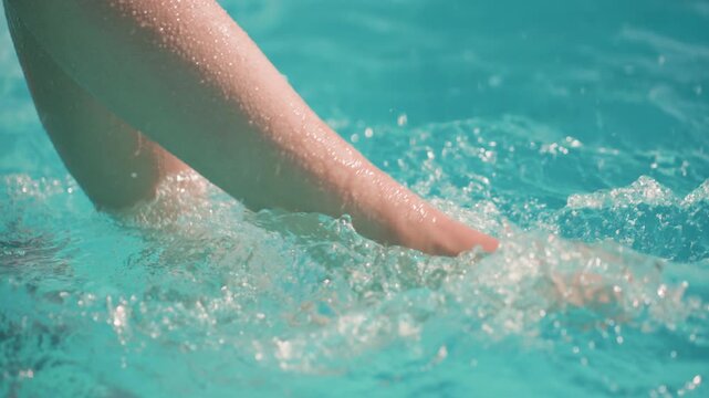 Woman legs and feet moving through clear blue water creating splashes. scene focuses on interaction between skin texture and liquid environment emphasizing fluid motion and aquatic setting