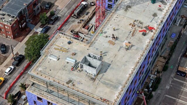 Aerial view of a construction site at Cherry Creek with workers on the concrete rooftop, a red crane, and building materials in Denver, Colorado, United States.