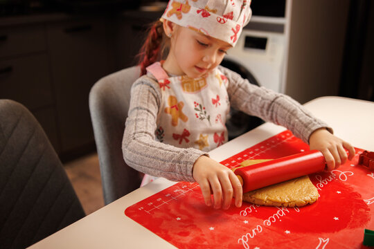 Child making festive Christmas cookies with a rolling pin at home.