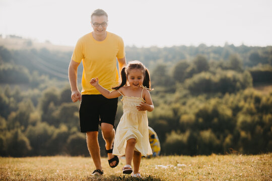 Father And Daughter Running Through Sunny Meadow Together During Summer Family Outdoor Play And Fun