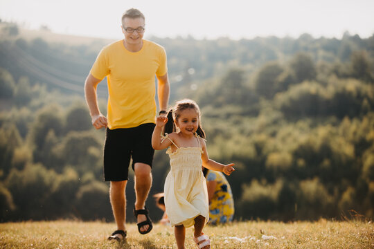 Father And Daughter Running Through Sunny Meadow On A Summer Family Outdoor Adventure