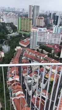 Aerial view of a cityscape featuring a mix of modern high-rise buildings and traditional houses with red roofs. Lush greenery surrounds the urban area.
