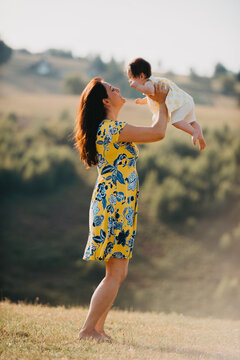 Mother Lifting Baby Outdoors In Sunny Countryside Field Showing Joyful Motherhood And Bonding