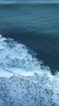 Waves crashing on a calm ocean surface. The water is deep blue with white foam at the crest of the waves. A serene coastal scene.