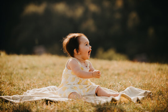 Joyful Baby Sitting on Blanket in Sunny Field Laughing and Playing Outdoors With Parent