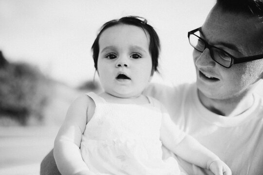 Father Holding Baby Daughter Outdoors in Black and White Family Portrait With Tender Smile