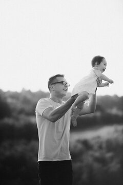 Father Lifting Baby Daughter Overhead During Outdoor Playful Moment, Smiling Parenthood And Family Bonding