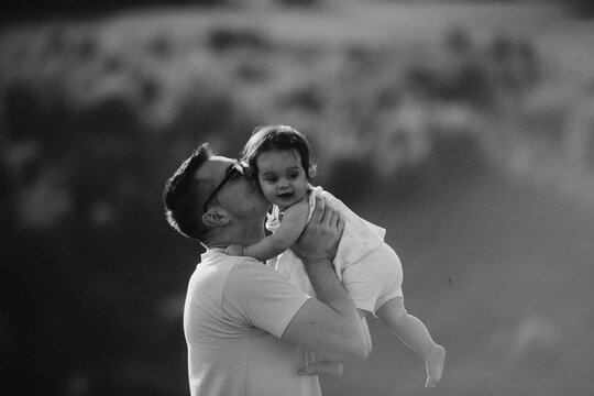Father Lifting And Kissing Baby Daughter Outdoors In Tender Black And White Family Portrait