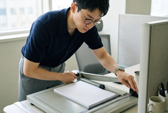 Generative AI, Asian man cutting paper with a guillotine paper cutter in the office