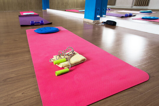 Bright pink yoga mats arranged in a modern fitness studio with colorful exercise equipment, jump ropes, towels and cushions, creating a vibrant wellness setting for yoga, stretching and workouts