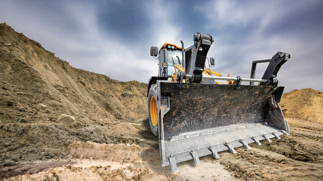 A universal excavator loader is at work moving earth on a construction site. The machine works in an area with piles of dirt and clear skies