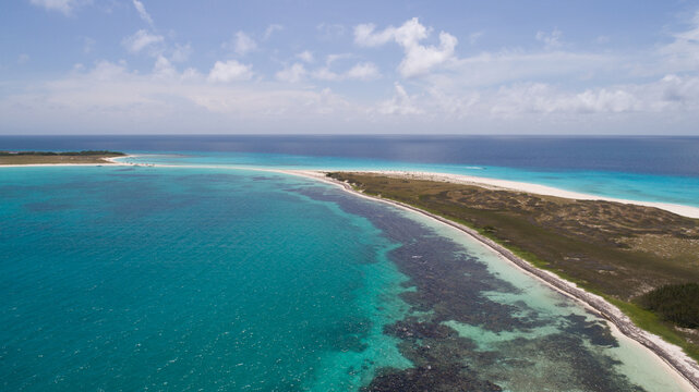 Aerial view of Los Roques archipelago featuring turquoise waters, coral reefs, and white sandy beaches under a clear blue sky in Los Roques, Dependencias Federales, Venezuela.
