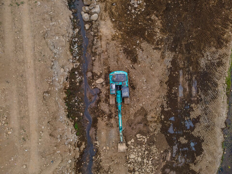 Aerial View of a Cyan-Colored Excavator Working in a Large-Scale Rock Ore Quarry Near a Steep Rocky Cliff in Dawuhan Kulon, Central Java, Indonesia. Active Mining and Rock Extraction from Above.