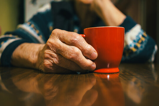 An elderly woman's hand is holding a red cup