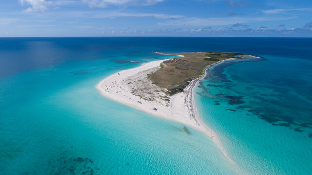 Aerial view of Los Roques archipelago featuring a pristine white sand beach, turquoise Caribbean waters, and coral reefs under a clear blue sky in Los Roques, Dependencias Federales, Venezuela.