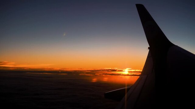 Airplane Wing Silhouette Against Orange Sunset Sky Above Clouds