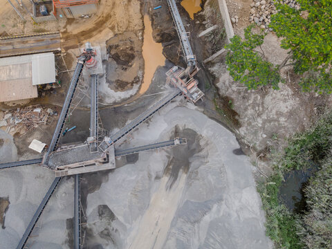 Rock Crusher Machine in the Middle of an Aggregate Stockpiling Area. Heavy Construction Machinery Is Surrounded by Rock, Sand, and Processed Materials in an Active Industrial Mining Site from Above.