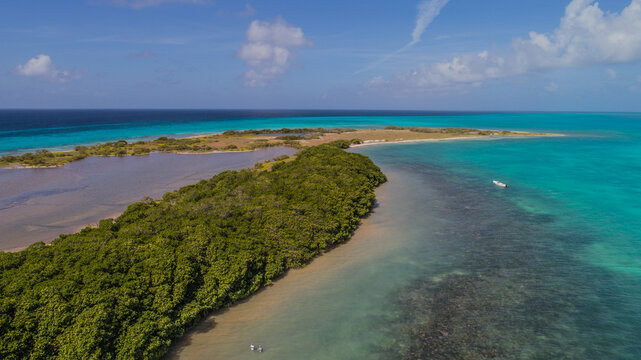 Aerial view of Los Roques archipelago with lush green vegetation, turquoise waters, and a small boat in the Caribbean Sea, Los Roques, Dependencias Federale, Venezuela.