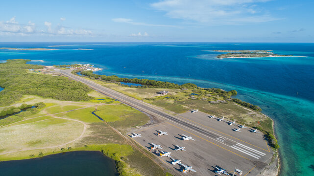 Aerial view of Los Roques airport runway with small aircraft on the tarmac, surrounded by turquoise Caribbean waters in Los Roques, Dependencias Federale, Venezuela.