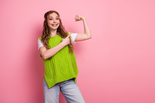 Young female student wearing green vest demonstrates confidence by flexing her arm and pointing set pink background fashion lifestyle stock photo