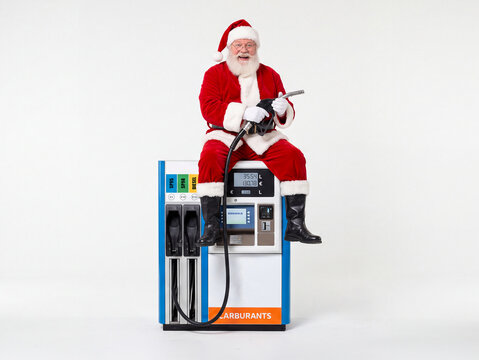 P&egrave;re No&euml;l assis sur une pompe &agrave; essence moderne et tenant un pistolet de carburant, isol&eacute; sur fond blanc