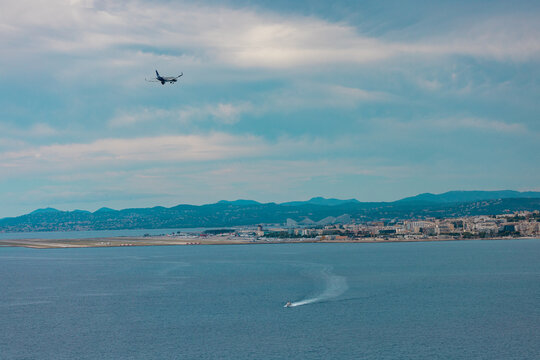 Aerial view of an airplane approaching Nice Cote d'Azur Airport over the Mediterranean Sea with a boat leaving a wake near the coastline of Nice, Provence-Alpes-Cote d'Azur, France.