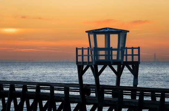 Luc-Sur-Mer, France - 08 08 2026:  View of a wooden pier in front of the sea, a colorful sunrise and port of Le Havre far away