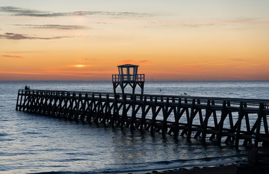 Luc-Sur-Mer, France - 08 08 2026:  View of a wooden pier in front of the sea, a colorful sunrise and port of Le Havre far away