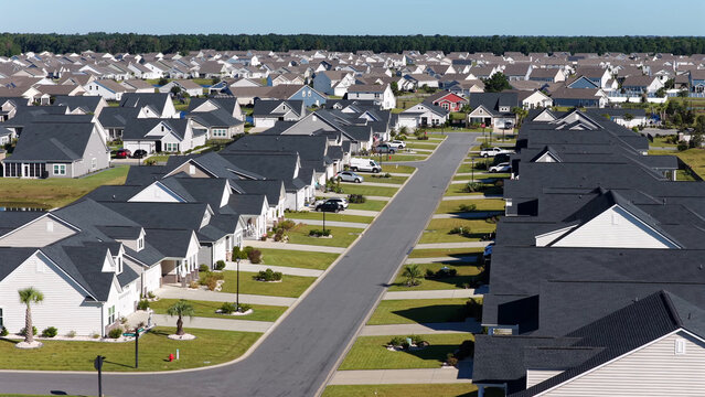 Aerial view of a suburban residential neighborhood with rows of houses featuring dark roofs, green lawns, and paved streets in Myrtle Beach, South Carolina, United States.
