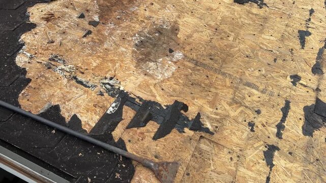 Close view shows torn roofing shingles and exposed wood decking as damaged material is cleared during residential roof repair preparation