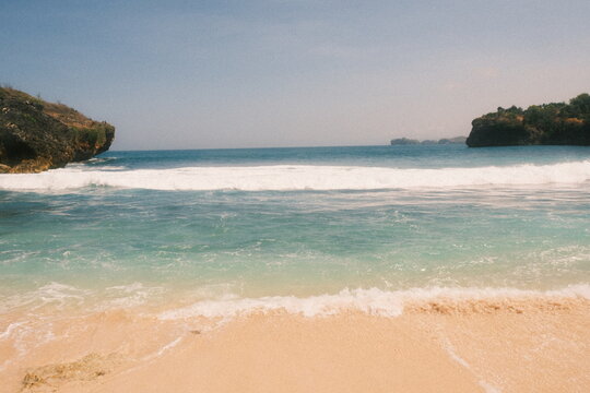 Waves rolling into a sandy cove between rocky headlands