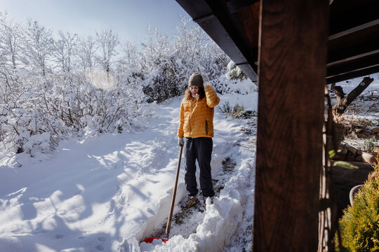 Tired caucasian woman shoveling snow near a country house terrace on a bright sunny winter day.