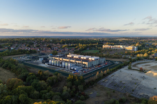 Aerial view of a modern data center facility surrounded by lush greenery and trees under a soft golden hour sky in the United Kingdom.
