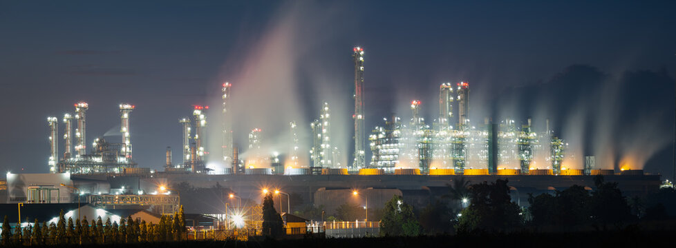 Panorama industrial refinery, gas fired power station at Map Ta Phut, Rayong, Thailand, with cooling system, process towers and illuminated plant, downward trend graph show energy market decline.