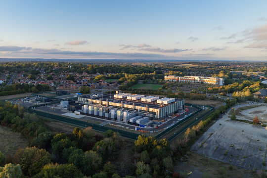 Aerial view of a modern data center facility surrounded by lush green trees and suburban residential areas in the United Kingdom.