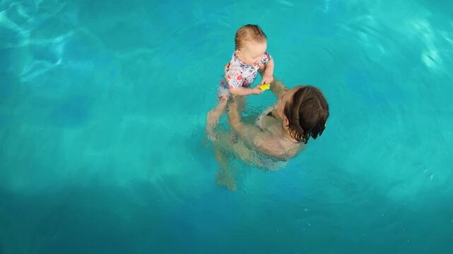 Mother holding baby in swimming pool top view