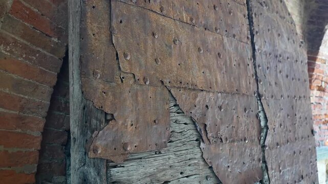Old wooden gate with rusted metal covering and downward tilt