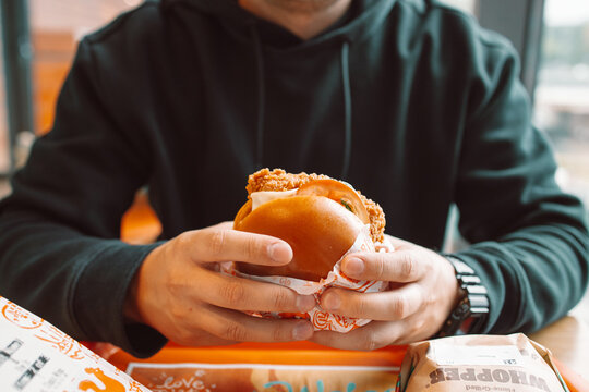 Close-up portrait of a young caucasian man holding a large delicious hamburger or cheeseburger, getting ready to take a bite in a modern restaurant interior. 