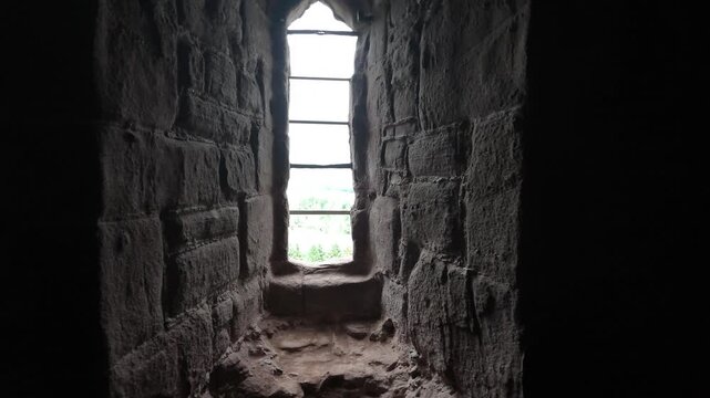 Smooth forward camera movement inside a dark medieval dungeon or fortress, approaching an old window with iron bars and stone walls