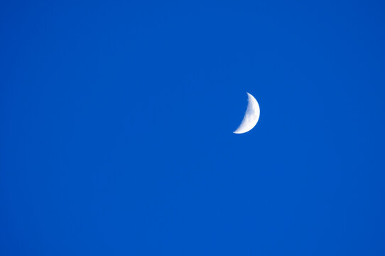 Small white crescent moon glowing against a clear deep blue sky, twilight sky landscape