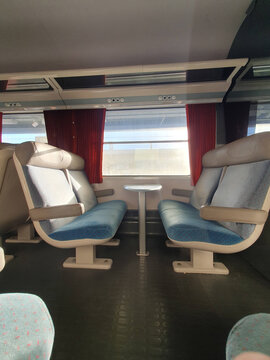Empty Train Interior With Paired Seats and Window Table, Sunlit Commuter Carriage With Red Curtains