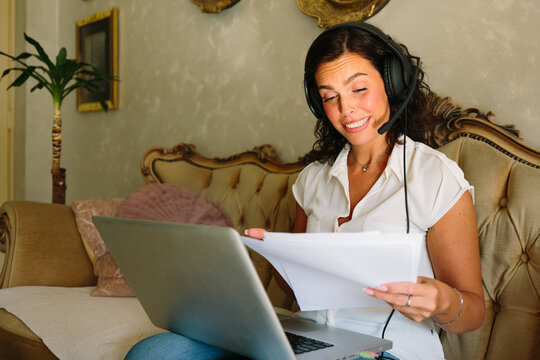 Woman reviewing paperwork while working remotely on laptop