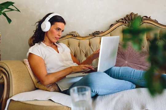 Woman working on laptop while listening through headphones at home