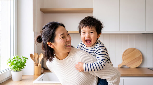 Happy mother and son playing and laughing in kitchen.  Joyful young mom piggyback her little boy having fun together at home